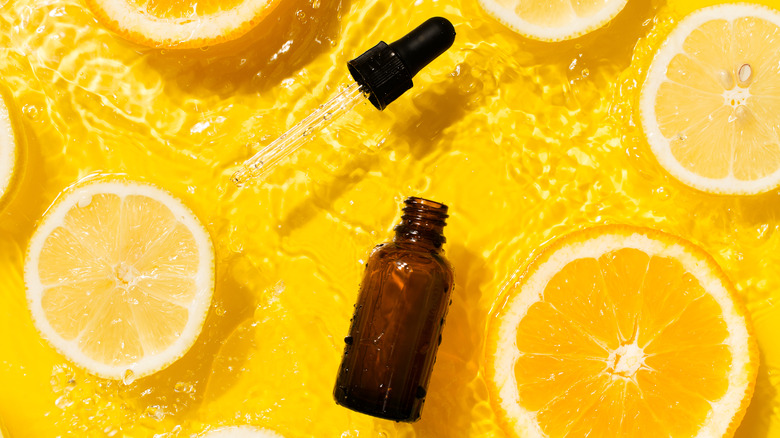 Open serum dropper bottle lying on top of water with a yellow background and lemon slices