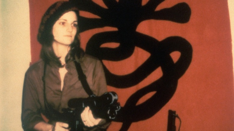 Patty Hearst holding a machine gun in front of a banner with the logo for the Sybionese Liberation Army