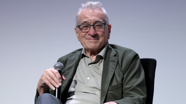 Robert De Niro smiling and holding a microphone at a film screening.