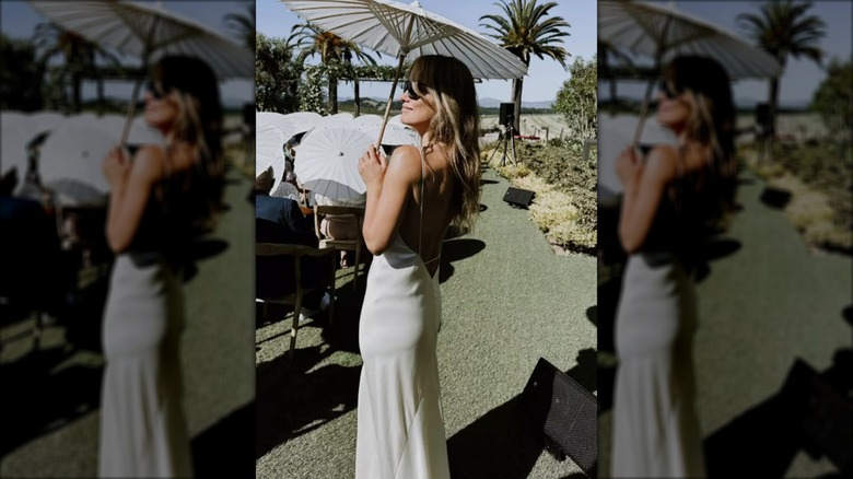 Screenshot from Olivia Wilde's Instagram Story of her wearing white and holding a white parasol at Colton Underwood and Jordan C. Brown's wedding