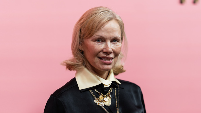 Pamela Anderson in black dress with tan collar and layered necklaces with short bob at 2025 Pandora Launch event
