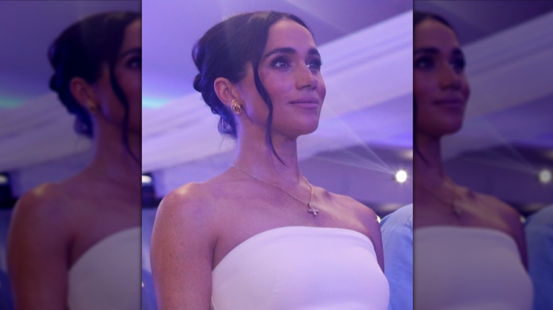 Closeup of Meghan Markle in white strapless dress and updo hairstyle with gold necklace and earrings