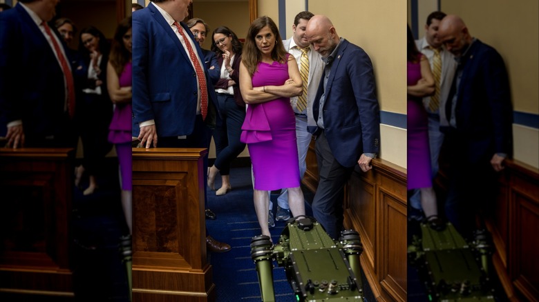 Nancy Mace with her arms crossed over her chest, surrounded by people, with a robot in front of her.