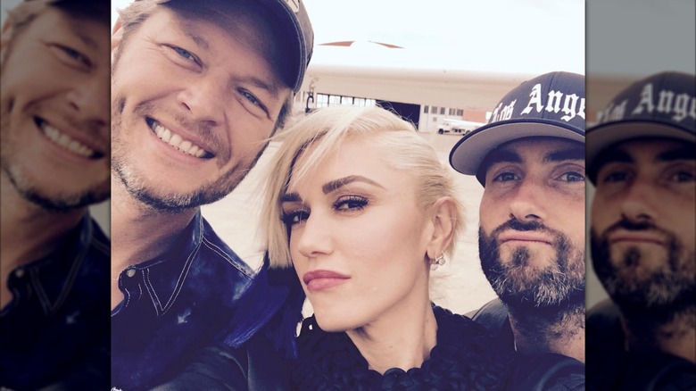 Gwen Stefani taking a selfie between Blake Shelton and Adam Levine on an airport tarmac