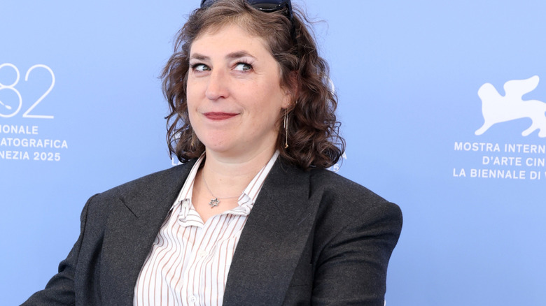 Mayim Bialik wearing sunglasses on top of her head and glancing to the side while smiling tightly
