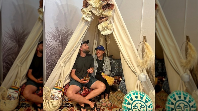 Mayim Bialik and Jonathan Cohen sitting inside a tepee-like structure