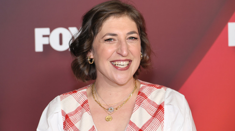 Malim Bialik laughing and wearing stacked necklaces and gold hoop earrings