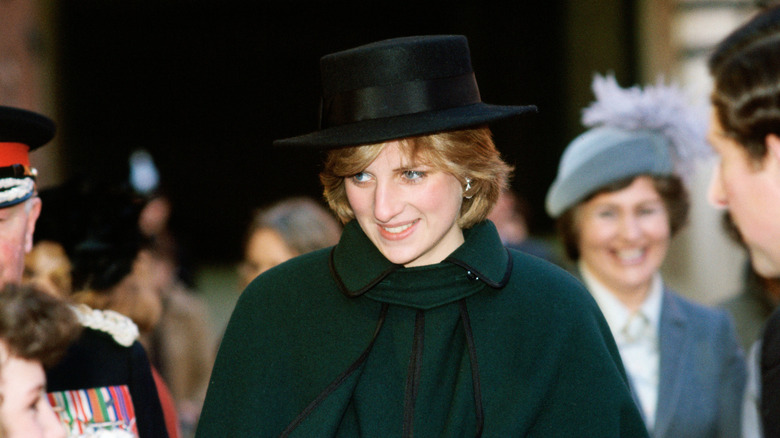 Princess Diana smiling in a green coat and black hat