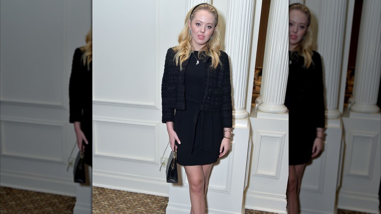 Tiffany Trump wearing a black jacket and matching minidress and posing in front of a white column
