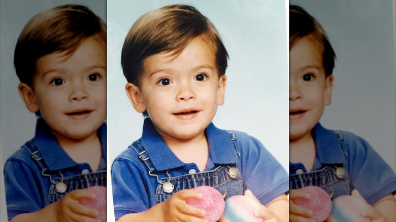 Michael Consuelos as a toddler smiling and wearing overalls