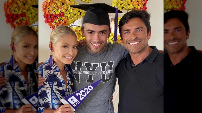 Michael Consuelos wearing a graduation cap and a NYU shirt in between Kelly Ripa and Mark Consuelos.
