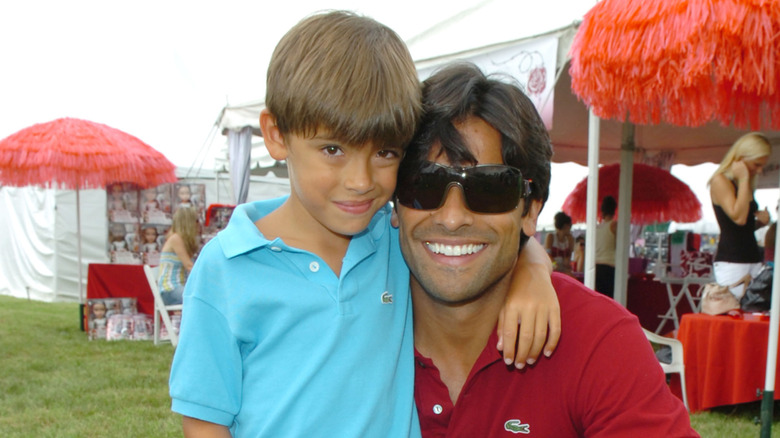 Michael Consuelos looking into the camera as a young child with his arm around Mark Consuelos' neck