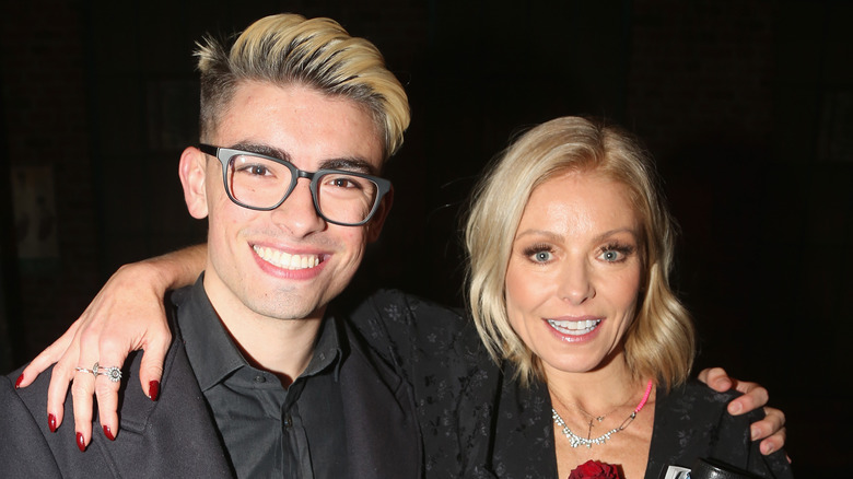 Michael Consuelos with blonde hair smiling with his arm around his mom, Kelly Ripa