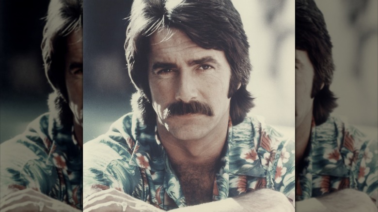 Sam Elliott posing for a photo circa 1975 wearing a floral print shirt
