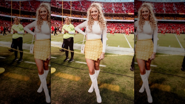 Brittany Mahomes with her legs crossed and her hand on her hip on the side lines.