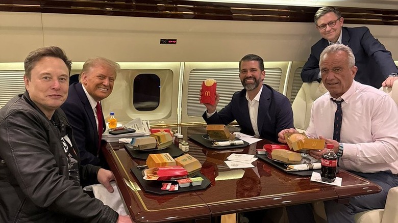 Elon Musk, Donald Trump, Donald Trump Jr., Robert F. Kennedy Jr., and Mike Johnson posing around a table of McDonald's food on Air Force One