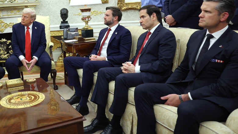 JD Vance, Marco Rubio, and Pete Hegseth seated on a couch beside Donald Trump seated in a chair in the Oval Office