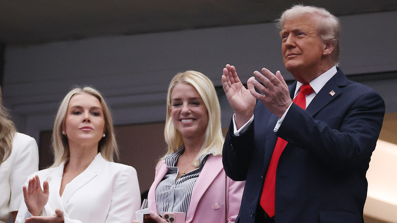 Donald Trump standing up and clapping beside Pam Bondi and Karoline Leavitt at the US Open