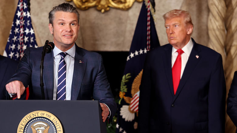 Donald Trump glares to the side beside Pete Hegseth as he speaks and points down at his lectern