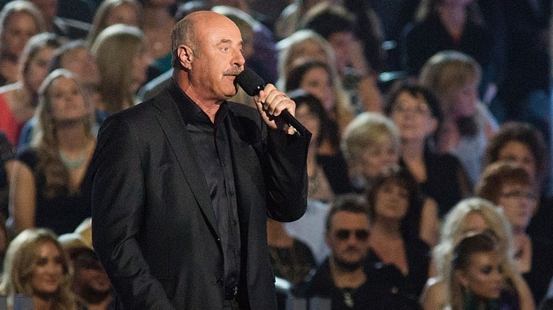 Dr. Phil holding a microphone in front of an audience