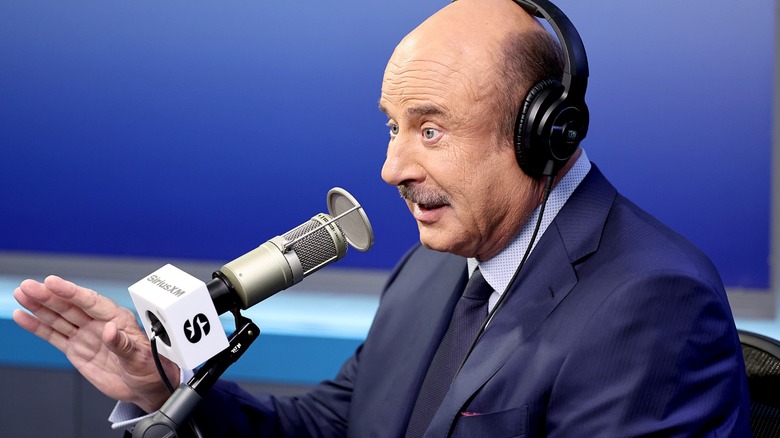 Dr. Phil with headphones on, speaking into a "Sirius XM" microphone