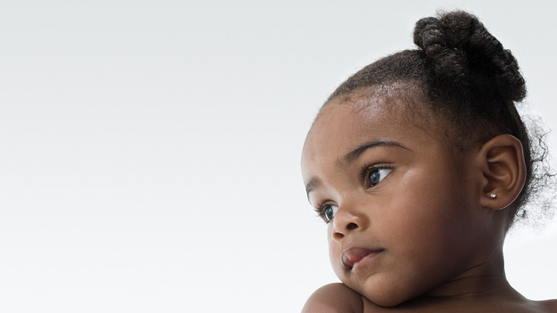 A baby girl looking to the side and wearing a high bun