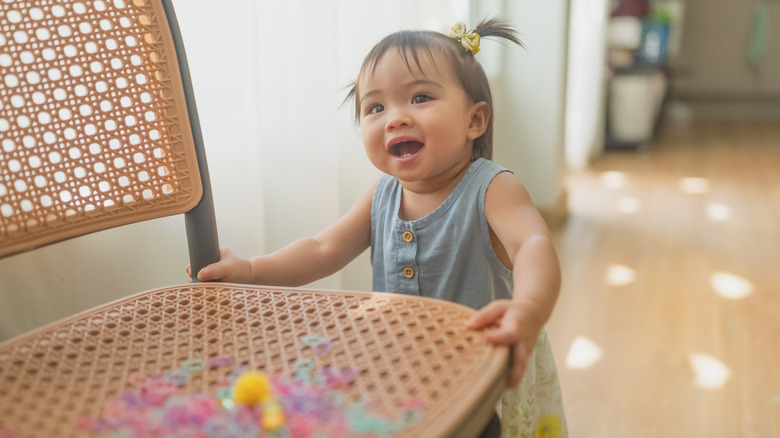 A baby girl with pigtails holding the seat of a chair