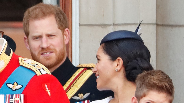 Meghan Markle in a blue hat turning around to talk to Prince Harry during Trooping the Color