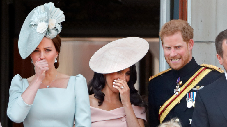 Meghan Markle smiling with her hand over her mouth while Kate Middleton covers her mouth