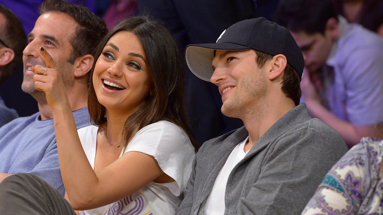 Ashton Kutcher and Mila Kunis laughing and pointing at a Los Angeles Lakers game at Staples Center in 2013