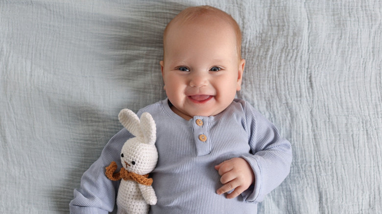 Aerial shot of a smiling baby resting on a gray blanket while holding a crochet bunny toy.