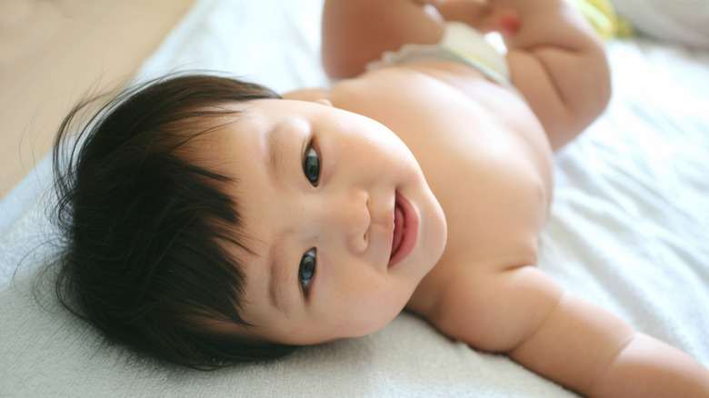Close-up photo of a baby lying atop a blue blanket while looking up at the camera.