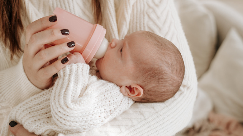 Photo of a woman holding a baby in her arms while the baby feeds from a baby bottle.