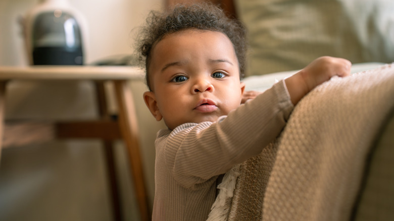 Photo of a baby gripping a blanket draped on a living room couch.