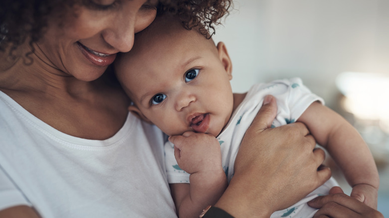 Photo of a woman looking down while holding a baby in her arms.