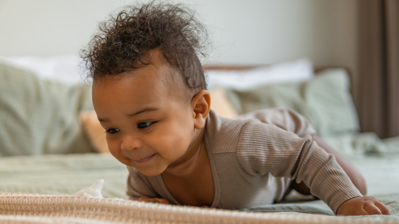 Photo of a baby lying on their tummy atop a bed.