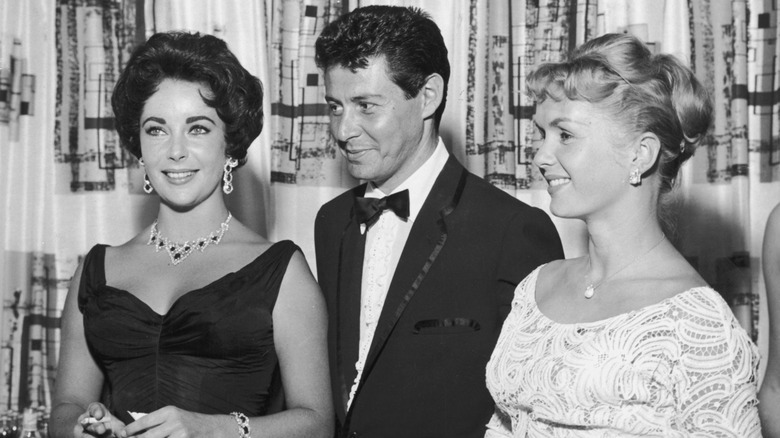 Eddie Fisher standing between Elizabeth Taylor and Debbie Reynolds; Eddie is looking at Liz