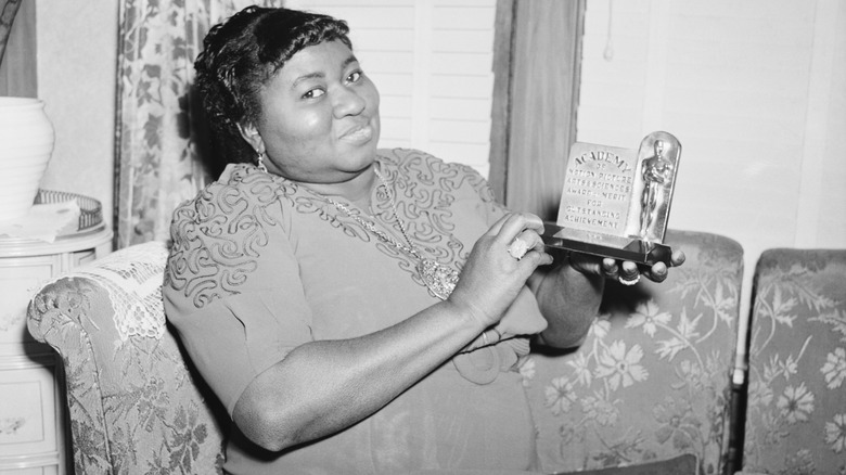 Hattie McDaniel sitting on a couch, holding up the plaque she received at the Oscars