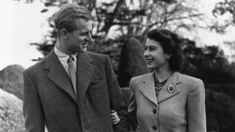 A young Prince Philip and Queen Elizabeth II linking arms and smiling at each other