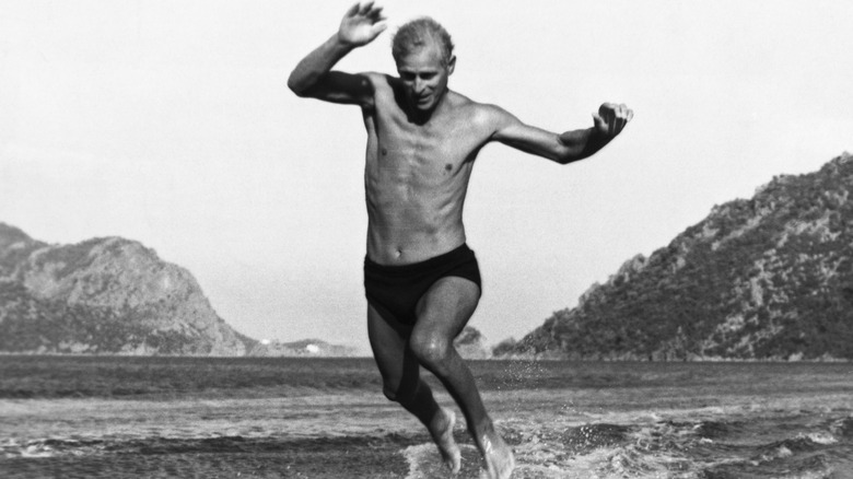A young Prince Philip in swimsuit jumping in water a the beach