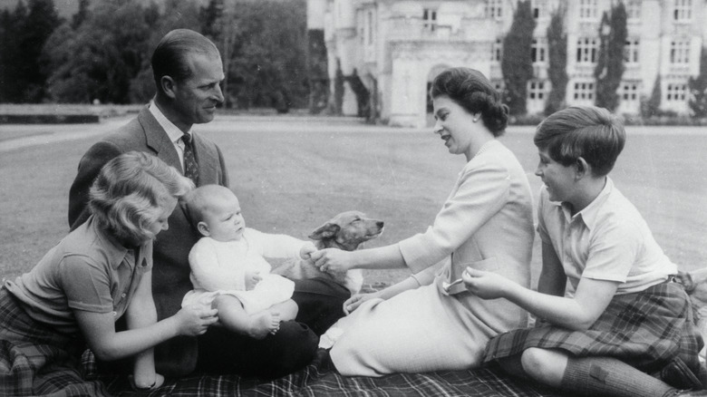 Prince Philip and Queen Elizabeth II sitting on a lawn with a young Prince Charles, Princess Anne, and an infant Prince Andrew