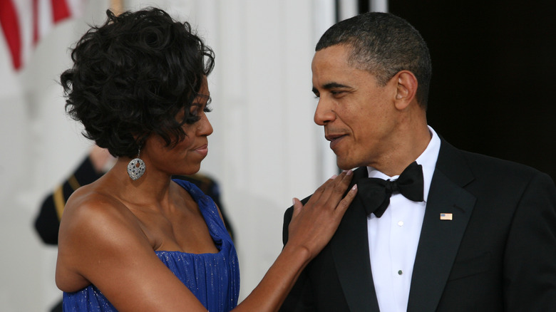 Michelle Obama and Barack Obama looking at each other in formal attire while the former puts her hand on Barack's shoulder