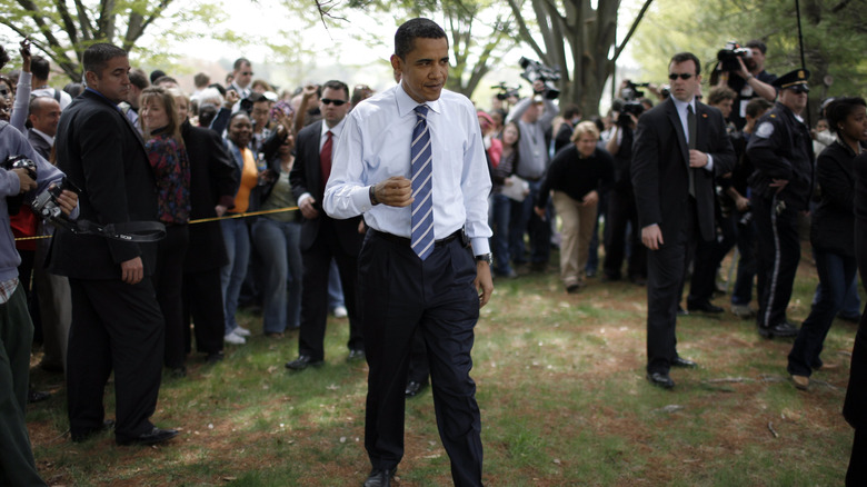 Barack Obama walking outside surrounded by crowds, press, and security