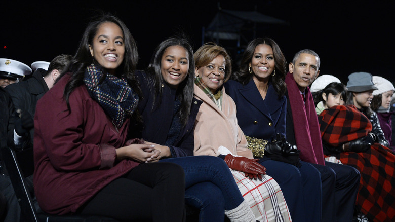 The Obama family with Marian Robinson smiling and sitting outside in an audience wearing coats and scarves
