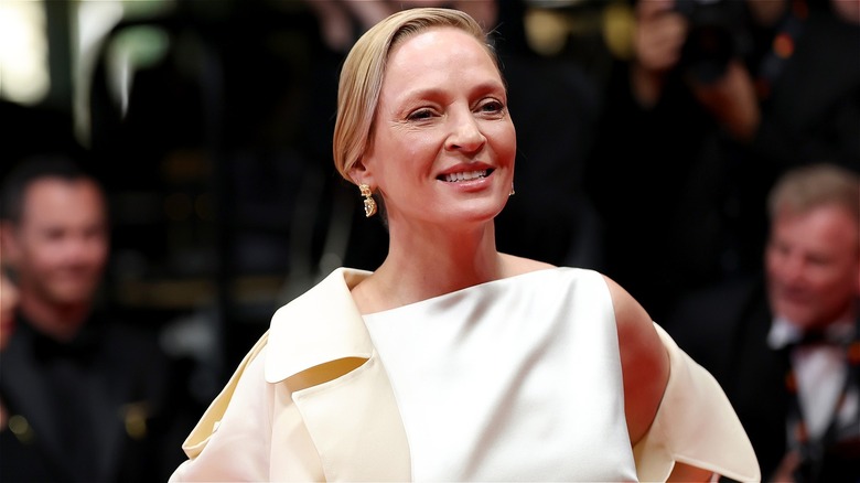 Uma Thurman smiling in a white dress and trench coat