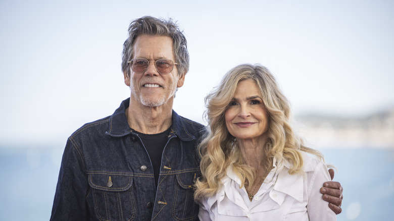Kevin Bacon in a denim shirt with an arm around Kyra Sedgwick