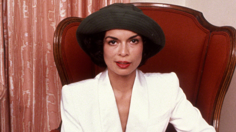 Bianca Jagger posing in a chair for a photo in 1981 wearing a white pantsuit