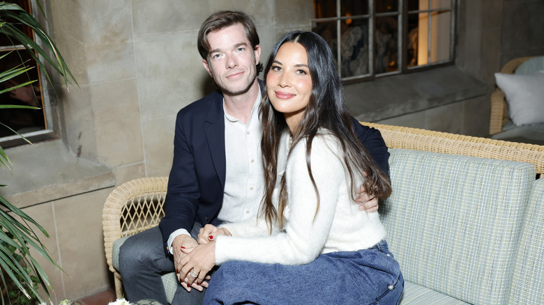 John Mulaney and Olivia Munn sitting holding hands