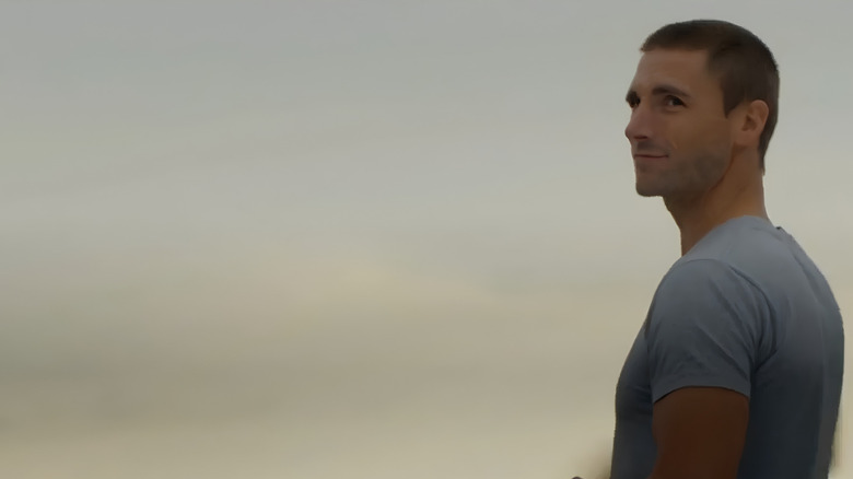 Screenshot of Hallmark movie "Bridal Wave" starring Andrew W. Walker. Walker is wearing a blue short-sleeved T-shirt and is staring gently at someone past the camera.