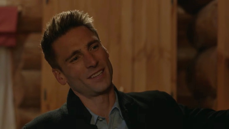 Screenshot of Hallmark movie "My Secret Valentine" starring Andrew W. Walker. Walker is smiling at something beyond the camera and is wearing a black coat and blue shirt with the top button undone.